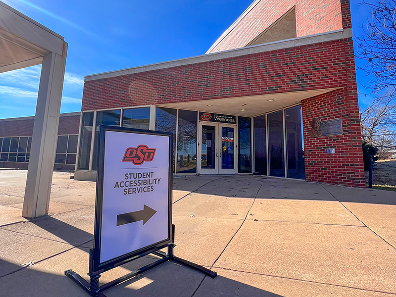 Sign in front of brick building that says Student Accessibility Services and points to the right Sign in front of brick building that says Student Accessibility Services and points to the right